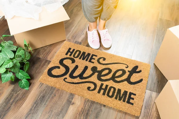 Vrouw in roze schoenen en zweten permanent in de buurt van Home Sweet Home Welkom Mat, dozen en Plant. — Stockfoto