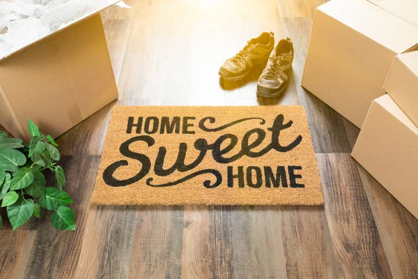 Otthon, édes otthon üdvözlő szőnyeg, mozgó dobozok, a cipők és a növény a kemény fa padló. — Stock Fotó