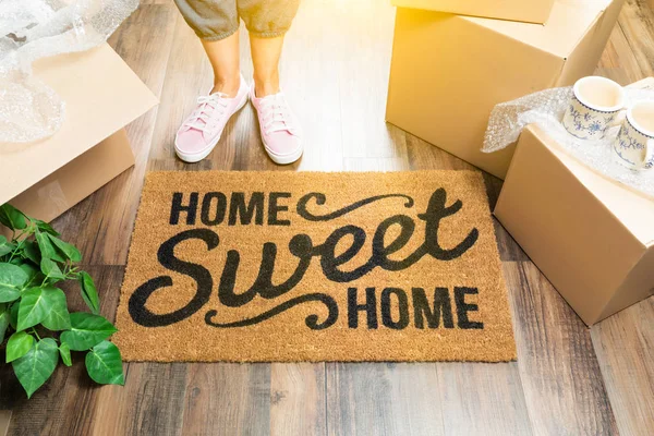 Woman in Pink Shoes and Sweats Standing Near Home Sweet Home Welcome Mat, Boxes and Plant. — Stock Photo, Image