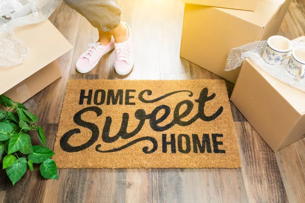 Woman in Pink Shoes and Sweats Standing Near Home Sweet Home Welcome Mat, Boxes and Plant. — Stock Photo, Image