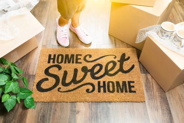 Woman in Pink Shoes and Sweats Standing Near Home Sweet Home Welcome Mat, Boxes and Plant. — Stock Photo, Image