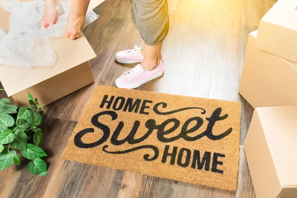 Vrouw in roze schoenen en zweten uitpakken in de buurt van Home Sweet Home Welkom Mat, Verhuisdozen en planten. — Stockfoto