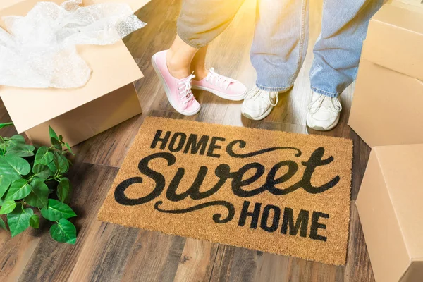 Mann und Frau stehen in der Nähe von zu Hause Sweet Home Willkommensmatte, Umzugskartons und Pflanzen. — Stockfoto