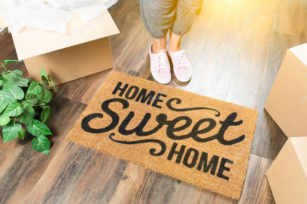 Woman in Pink Shoes and Sweats Standing Near Home Sweet Home Welcome Mat, Boxes and Plant.