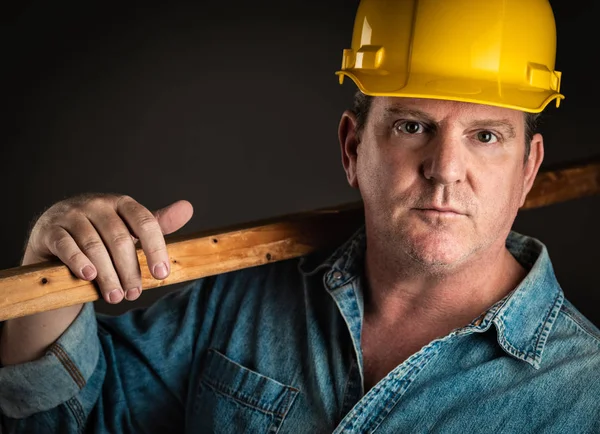 Serious Contractor in Hard Hat Holding Plank of Wood With Dramatic Lighting. — Stock Photo, Image