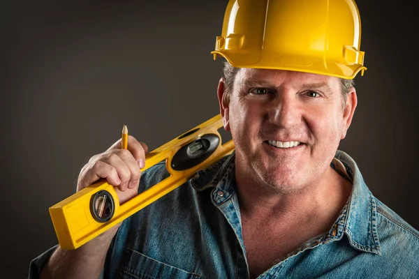 Lachende aannemer in Hard Hat Holding niveau en potlood met dramatische verlichting. — Stockfoto