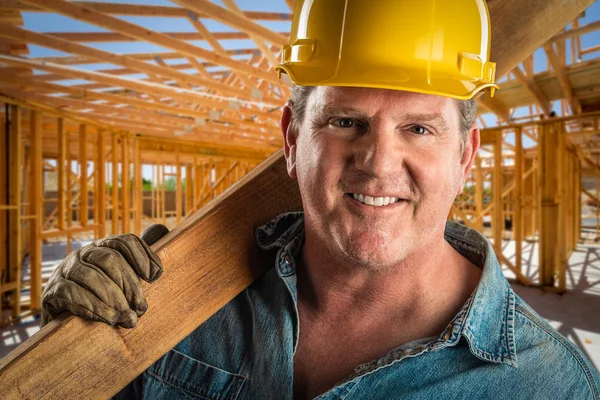 Lächelnder Bauunternehmer mit Bollenhut hält Holzplanke auf Baustelle. — Stockfoto
