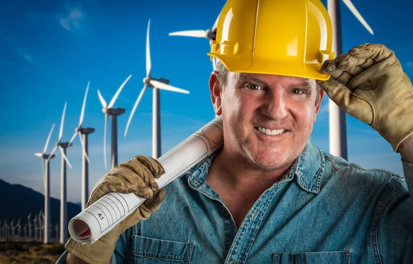 Uśmiechający się wykonawca w kask trzyma przedłużacz kabla na zewnątrz w pobliżu turbin wiatrowych. — Zdjęcie stockowe