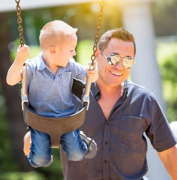 Felice giovane ragazzo avendo divertimento su il altalene con suo padre a il parco giochi . — Foto Stock
