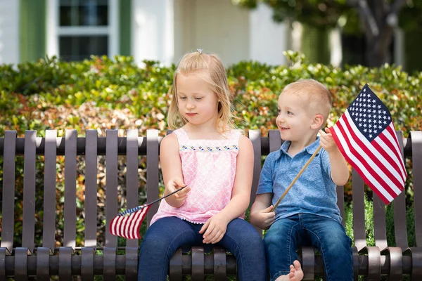 Молодая сестра и брат сравнивают друг друга по размеру американского флага на скамейке в парке . — стоковое фото