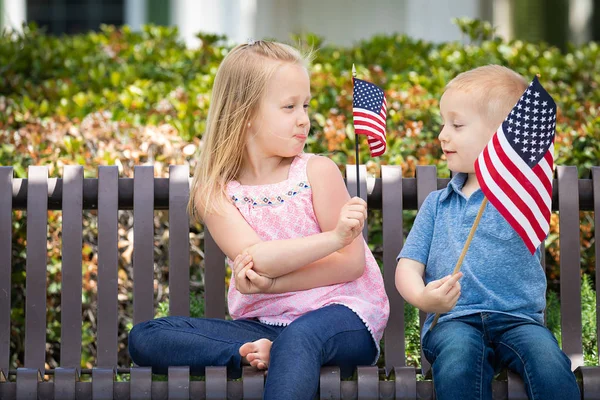 Kleine Schwester und Bruder beim Vergleich der amerikanischen Flaggengröße auf der Parkbank. — Stockfoto