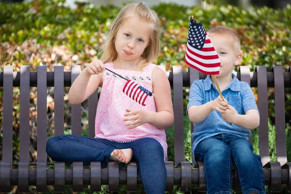 Kleine Schwester und Bruder beim Vergleich der amerikanischen Flaggengröße auf der Parkbank. — Stockfoto