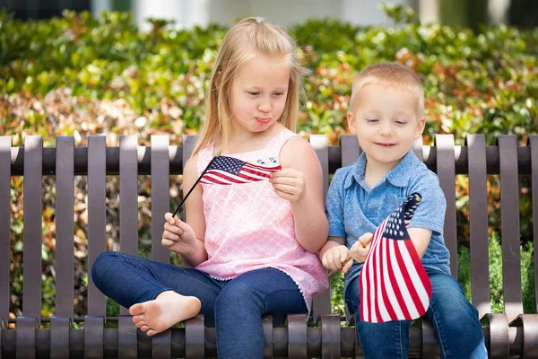 Hermana joven y hermano comparándose tamaño de la bandera americana en el banco en el parque . — Foto de Stock