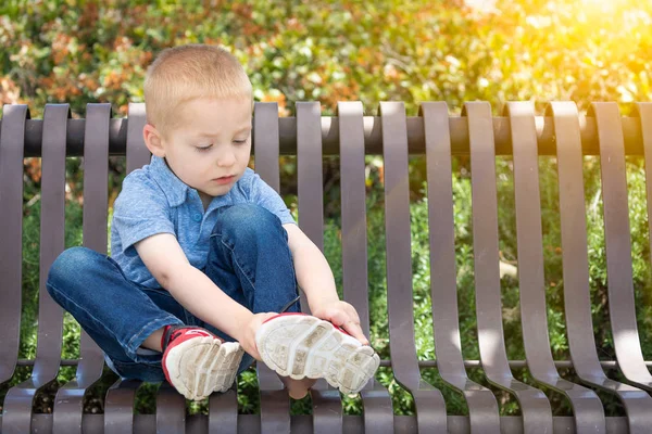 坐在长凳上的小男孩在公园穿上他的鞋子 — 图库照片