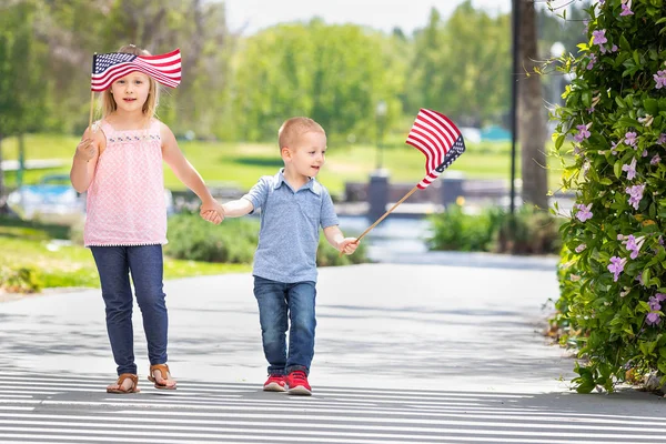 Kleine Schwester und Bruder schwenken amerikanische Flaggen im Park — Stockfoto