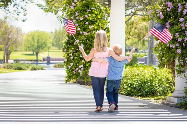 Kleine Schwester und Bruder schwenken amerikanische Flaggen im Park — Stockfoto