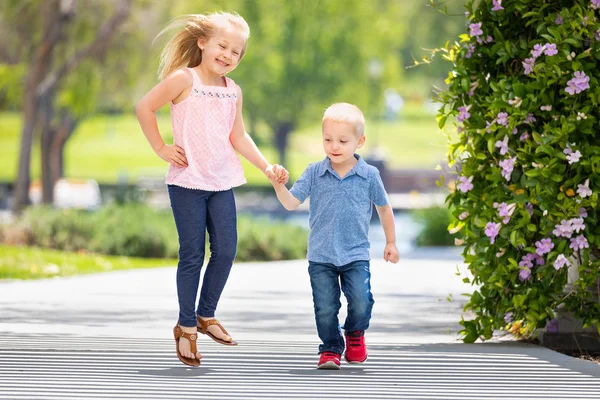 Молодая сестра и брат держатся за руки и бегают по парку — стоковое фото