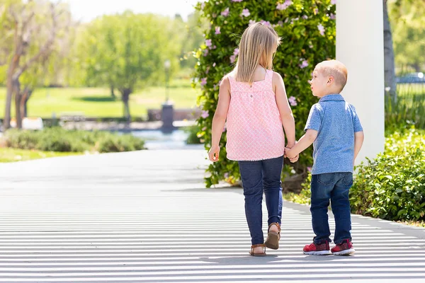 Молодая сестра и брат держатся за руки и ходят по парку — стоковое фото
