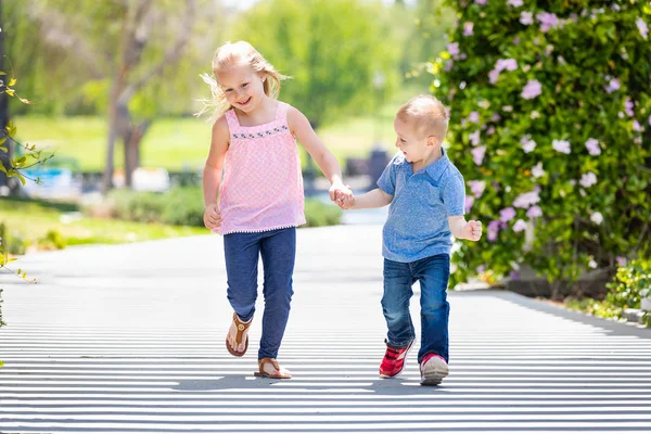 Irmã e irmão segurando as mãos e correndo no parque — Fotografia de Stock