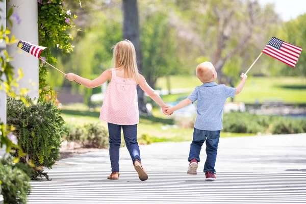 Mladá sestra a bratr držení rukou a mává americké vlajky v parku. — Stock fotografie