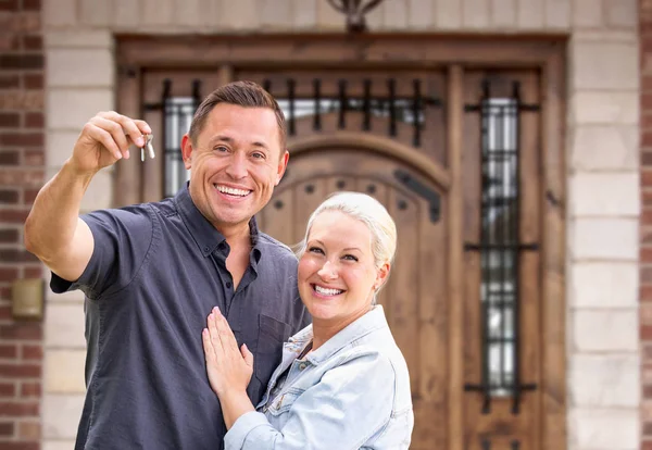 Casal jovem na frente da porta da frente da nova casa segurando chaves — Fotografia de Stock