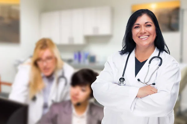 Knappe Spaanse dokter of verpleegster staand in haar kantoor met personeel achter de rug — Stockfoto
