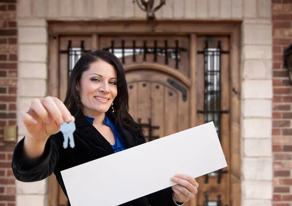 Іспаномовна жінка тримає чистий знак і ключі перед будинком — стокове фото