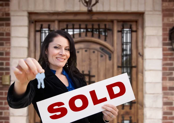 Spaanse vrouw houdt Verkocht teken en sleutels in de voorkant van huis — Stockfoto