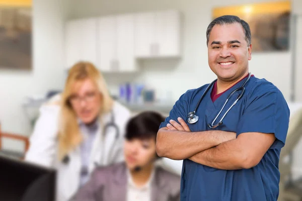 Knappe Spaanse dokter of verpleegster die in zijn kantoor staat met personeel achter de hand — Stockfoto