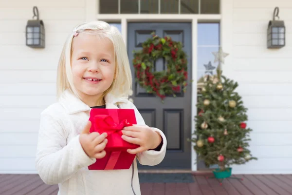 Söt ung flicka med gåva på verandan av hus med juldekorationer. — Stockfoto