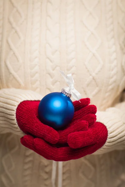 Mulher vestindo luvas vermelhas sazonais segurando ornamento de Natal azul — Fotografia de Stock