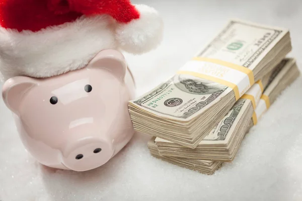 Piggy Bank vestindo chapéu de Santa perto de pilhas de notas de cem dólares em flocos de neve — Fotografia de Stock