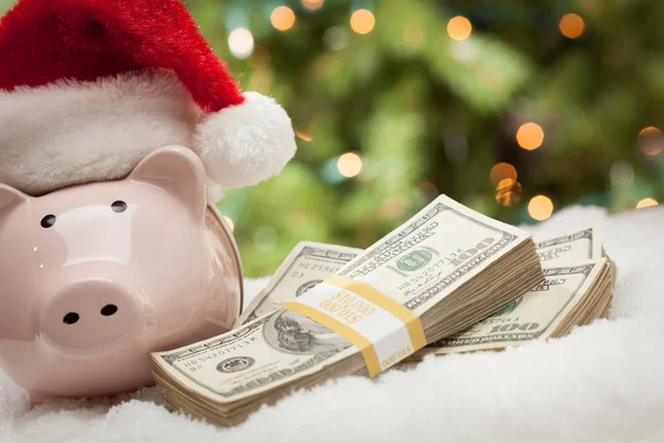 Piggy Bank w Santa Hat w pobliżu stosów studolarowych banknotów na płatkach śniegu — Zdjęcie stockowe