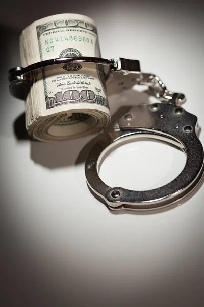 Handcuffs Locked on Roll of One Hundred Dollar Bills Under Spotlight — Stock Photo, Image