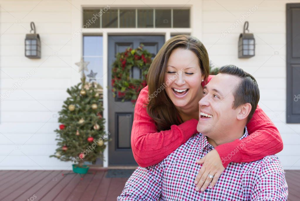 Happy Young Couple Laughing On Front Porch of House With Christmas Decorations.