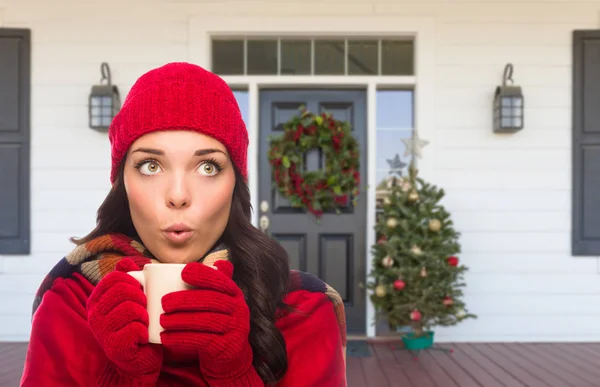 Junges Mädchen mit Schal, roter Mütze und Handschuhen mit heißem Kakao-Becher steht auf der weihnachtlich dekorierten Veranda — Stockfoto