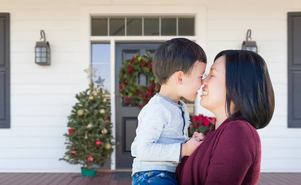 Mama chineză și cursa mixtă pentru copii frecarea nasurilor în picioare pe veranda frontală decorată de Crăciun — Fotografie, imagine de stoc