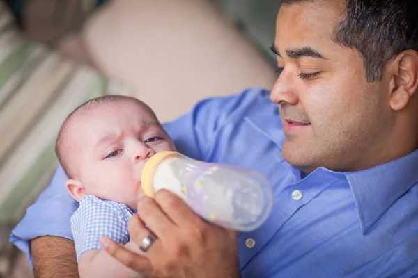 Feliz padre hispano biberón alimentar su muy contenido mezclado raza bebé hijo — Foto de Stock