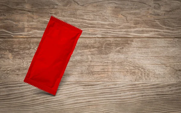 Blank Red Condiment Packet Floating on Aged Wood Background — Stock Photo, Image