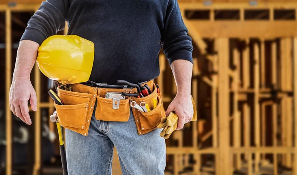 Entrepreneur avec ceinture à outils et casque de sécurité devant le chantier de construction à ossature de bois — Photo