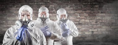 Chinese Woman and Team Behind In Hazmat Suites, Gas Masks and Goggles Against Brick Wall clipart