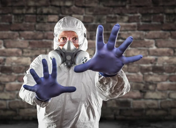 Hombre con traje de materiales peligrosos, máscara de gas protectora y gafas que alcanzan a parar con las manos —  Fotos de Stock