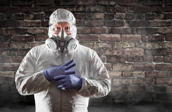 Hombre con traje de materiales peligrosos, máscara protectora de gas y gafas contra la pared de ladrillo —  Fotos de Stock