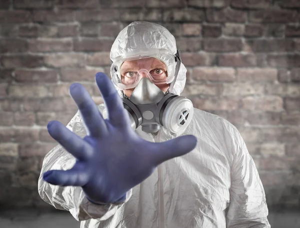 Homem vestindo terno Hazmat, máscara de gás de proteção e óculos chegando com parede de tijolo de mão atrás — Fotografia de Stock