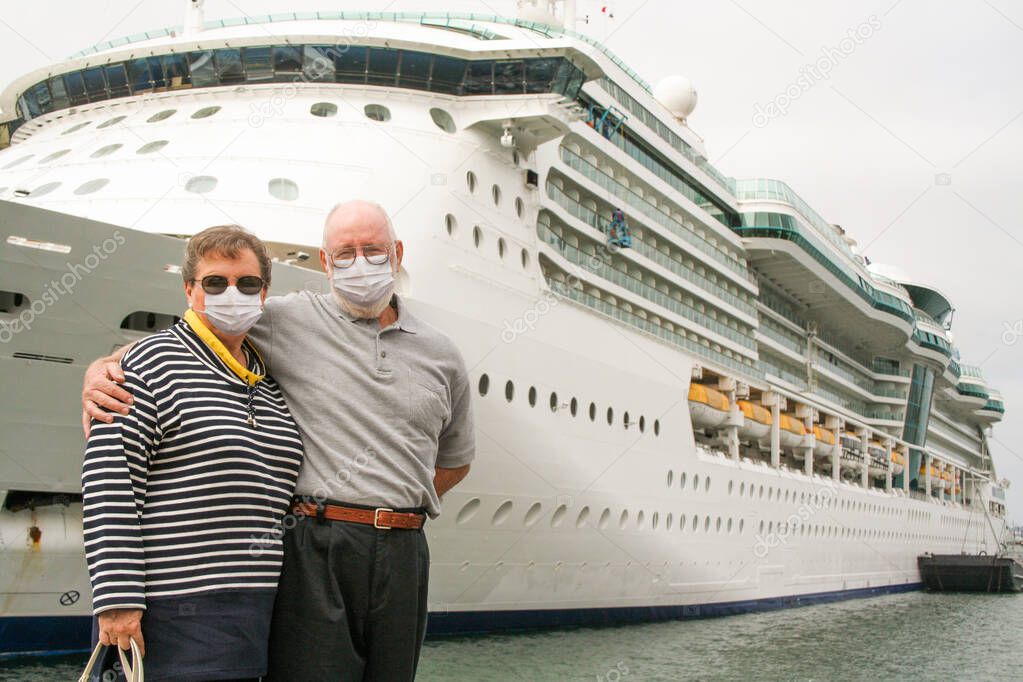 Senior Couple Wearing Face Masks Standing In Front of Passenger Cruise Ship.