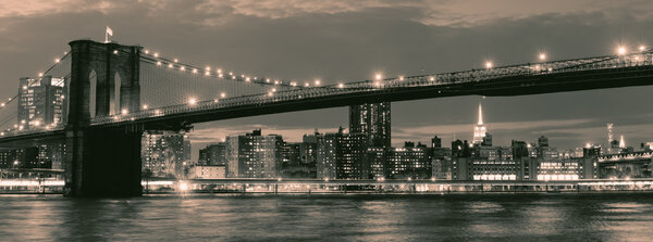 Vintage image of the Brooklyn Bridge illuminated at night with reflections on the East River