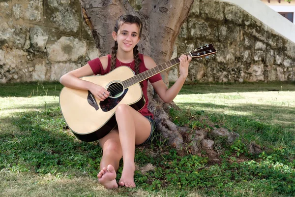Adolescente bastante hispana tocando una guitarra acústica sentada — Foto de Stock