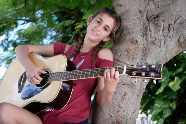 Pretty hispanic teenage girl playing an acoustic guitar sitting — Stock Photo, Image