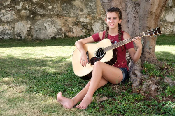 Adolescente bastante hispana tocando una guitarra acústica sentada — Foto de Stock