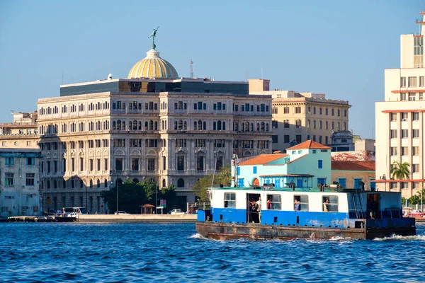 Ein altes motorboot bringt passagiere durch die bucht von havana mit bunten gebäuden im hintergrund — Stockfoto